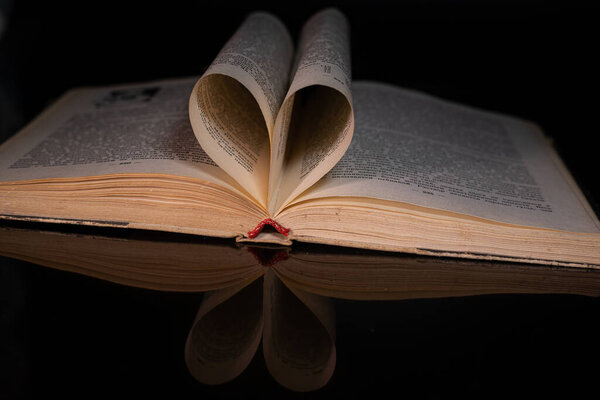Old book with pages folded into a heart shape on a black background. Valentine's Day.