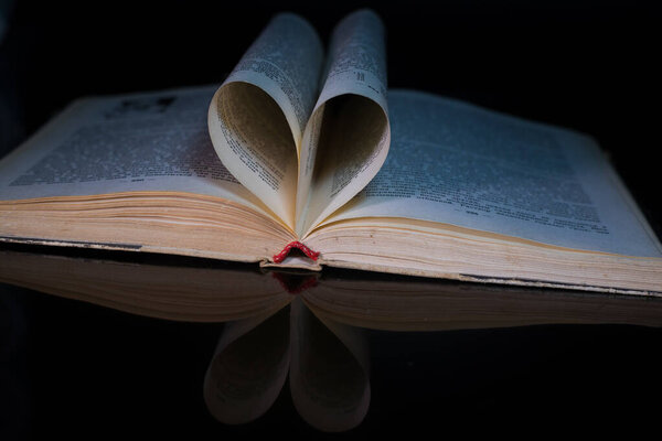 Old book with pages folded into a heart shape on a black background. Valentine's Day.