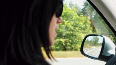 Bir kadın araba sürüyor ve yolda giderken aynaya bakıyor..
