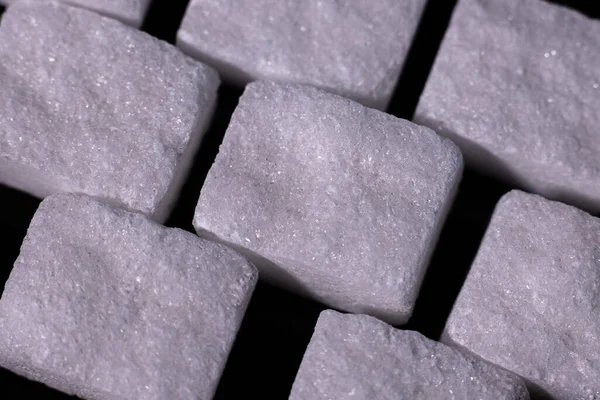 Squares of sugar cubes on a black background. Diabetes. Sugar disease.