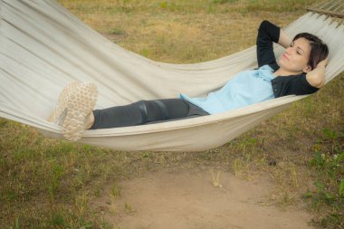 Bir kadın hamakta oturuyor. Tatil eğlencesi. Evin bahçesinde, doğaya yakın bir rahatlama..