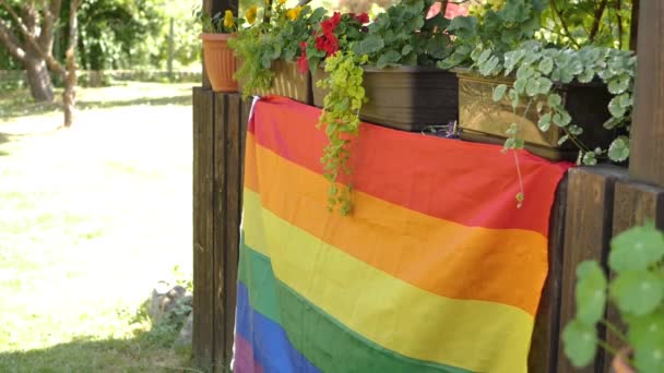 庭では 夏の葉のテラスにLgbtの旗が置かれ 木の風にゲイの誇り虹の旗がなびく 庭のパーティー — ストック動画