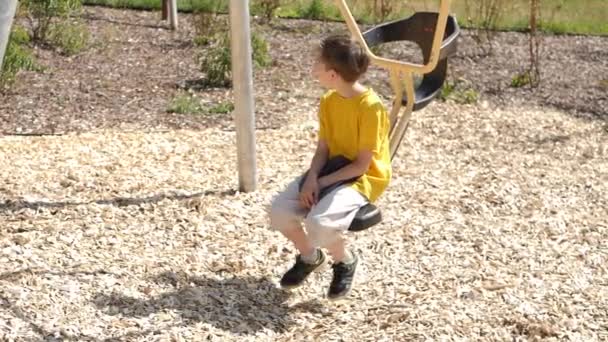暑い夏に子供の遊び場でスイングする男の子 ビデオだ 柔らかい選択的フォーカス — ストック動画