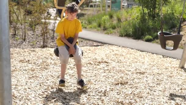 暑い夏に子供の遊び場でスイングする男の子 ビデオだ 柔らかい選択的フォーカス — ストック動画