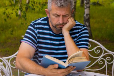 Bir adam dışarıda bir masada kitap okuyor. Adam dinleniyor. Yumuşak seçici odak.