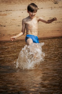 Boy running and splashing with water, summer vacation. Soft selective focus. clipart