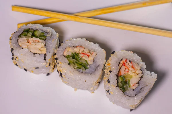 Nori yaprakları, pilav, salatalık, somon balığı suşi çeşitleri. Sushi, yemek çubuklarıyla beyaz bir arka plan tabağında yuvarlanıyor. Karışık seçmeli odak.