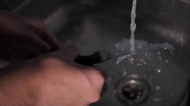 Adamın musluktan suyu akıyor. Bıçağı akan suda yıka. Yumuşak seçici odaklanma. Video klibi.