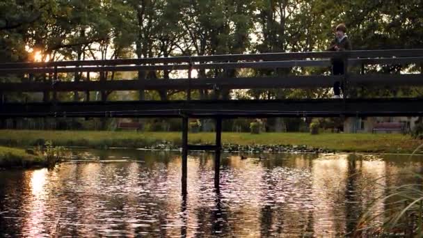 Jezioro Mostem Zachodzie Słońca Dzieci Moście Wrzucają Kamienie Wody Delikatne — Wideo stockowe