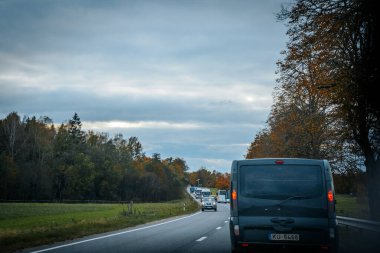 Şehir sonbahar yeşilliklerinden geçiyor: otoyolda ağaçlarla çevrili bir araba. Sonbahar yaprakları ormanında akşam gezisi. Yumuşak seçici odak.