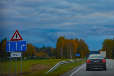 Şehir, ağaçlarla çevrili otobanda sonbahar yeşillik arabasının içinden geçiyor. Akşamları bulutlar kararır. Sonbahar yaprakları ormanında akşam gezisi. Yumuşak seçici odak. 