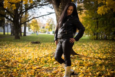Bir kadın şık bir kıyafetle parkta sonbahar yürüyüşünden zevk alır. Mutlu kadın sonbahar parkında boş vakit geçiriyor. Siyah deri elbiseli bir kadın..