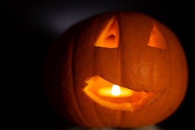 Cadılar Bayramı 'nda balkabağı oyuldu. Siyah arka planda yanan mum ışığı var. Parlak, renkli turuncu bir nesne, sade siyah bir zemin üzerinde, minimum ışıklandırmayla..