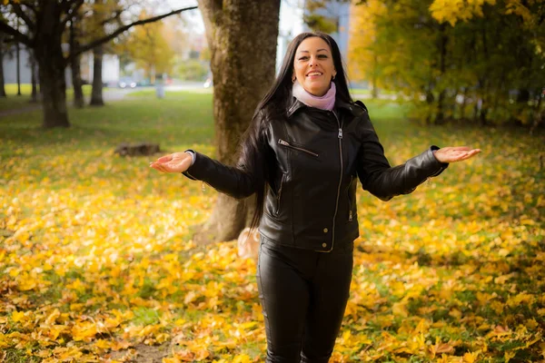 Bir kadın şık bir kıyafetle parkta sonbahar yürüyüşünden zevk alır. Mutlu kadın sonbahar parkında boş vakit geçiriyor. Siyah deri elbiseli bir kadın..