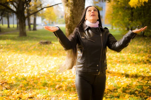 A woman enjoys an autumn walk in the park, in stylish outerwear. Happy woman enjoying free time in autumn park. A woman poses in black leather clothing.