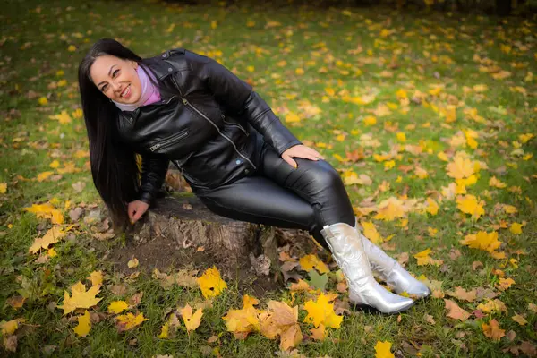 A woman enjoys an autumn walk in the park, in stylish outerwear. Happy woman enjoying free time in autumn park. A woman poses in black leather clothing.