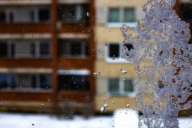 Kışın camda beyaz kar. Pencereye kar yağdı. Evin pencerelerini görebiliyorsun. Yumuşak seçici odak.