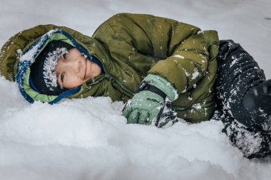 Kar yığınının içinde bir çocuk. Karda yatan biri kar meleği yapar. Karlı bir arazide kar meleği yapan bir adam.