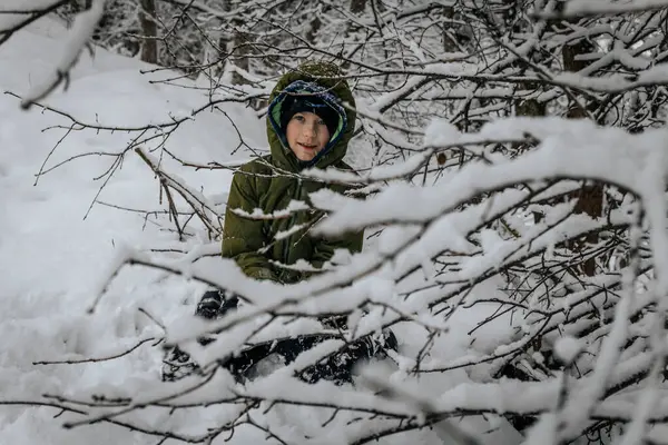 Boy in warm clothes near winter snowy trees. A child in warm clothes stands and looks at beautiful trees. Soft selective focus.