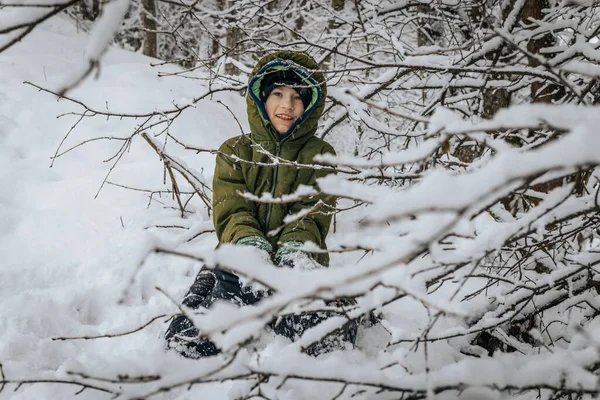 Boy in warm clothes near winter snowy trees. A child in warm clothes stands and looks at beautiful trees. Soft selective focus.