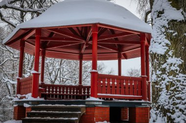 Kış kırmızı ahşap bir gölgelikle. Soğuk mevsimde karlı ağaçlar için kış. Eğlence parkında ağaç yaprakları..