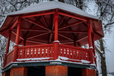 Kış kırmızı ahşap bir gölgelikle. Soğuk mevsimde karlı ağaçlar için kış. Eğlence parkında ağaç yaprakları..