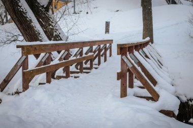 Nehir-gauja 'da kış manzarası. Çıplak ağaçlarda kar, sakin bir kış manzarasında. Buzlu nehir. Kışın tahta köprü.