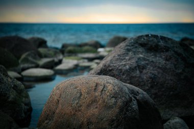 Baharda gün batımının ufukta göründüğü kasvetli deniz. Deniz kıyısındaki taşlar. Yumuşak seçici odaklanma. Resim için yapay olarak tahıl oluşturuldu