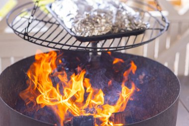 Folyoyla sarılmış yiyecek, dairesel ızgaranın üstünde ızgara yapıyor. Folyo paketleri bir fırın tepsisine konur ve alevler aşağıda görülebilir. Açık hava yemekleri ve barbekü meraklıları için mükemmel.. 