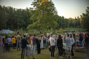 Neşeli bir topluluk güneşli bir günde ferah bir parkta toplanır. İnsanlar yeşil çimlere dağılmış, bazıları köpeklerini gezdiriyor, sosyalleşiyorlar ve dışarıda eğleniyorlar.. 