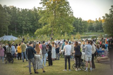 Neşeli bir topluluk güneşli bir günde ferah bir parkta toplanır. İnsanlar yeşil çimlere dağılmış, bazıları köpeklerini gezdiriyor, sosyalleşiyorlar ve dışarıda eğleniyorlar.. 