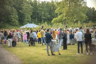 Neşeli bir topluluk güneşli bir günde ferah bir parkta toplanır. İnsanlar yeşil çimlere dağılmış, bazıları köpeklerini gezdiriyor, sosyalleşiyorlar ve dışarıda eğleniyorlar.. 