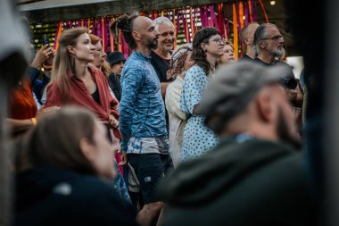 Çeşitli bir grup insan Valmiermuia Etnik Müzik Festivali 'nde birbirlerine yakın durup dikkatle izliyorlar.