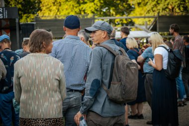 Çeşitli bir grup insan Valmiermuia Etnik Müzik Festivali 'nde birbirlerine yakın durup dikkatle izliyorlar.