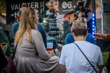 Meşgul bir seyirci bir etnik müzik festivalinde çimlerin üzerinde oturur ve etkinliği dikkatle izler. Kalabalık her yaştan insanı eğlendiriyor.