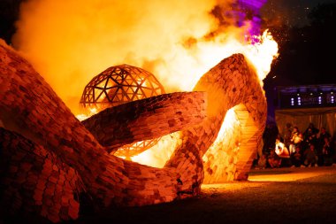 Görkemli bir ateş, büyük bir ahşap sanat tesisini gece sarar. Ahşap heykel, alevler ve dumanlar sahneyi aydınlatır.. 