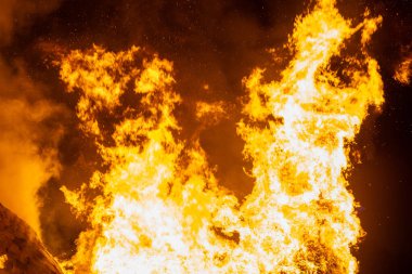 Büyük bir alev ahşap yapıyı yutar ve alevler gece gökyüzüne yükselir. Yoğun ateş, yangının yıkıcı gücünü gösteren sahneyi aydınlatıyor..