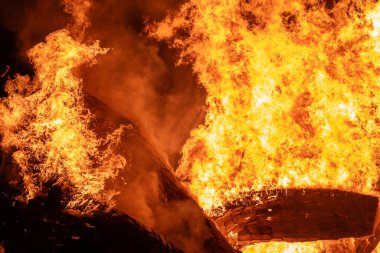 Büyük bir alev ahşap yapıyı yutar ve alevler gece gökyüzüne yükselir. Yoğun ateş, yangının yıkıcı gücünü gösteren sahneyi aydınlatıyor..