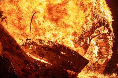 Büyük bir alev ahşap yapıyı yutar ve alevler gece gökyüzüne yükselir. Yoğun ateş, yangının yıkıcı gücünü gösteren sahneyi aydınlatıyor..