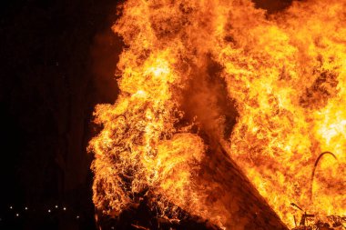 Büyük bir alev ahşap yapıyı yutar ve alevler gece gökyüzüne yükselir. Yoğun ateş, yangının yıkıcı gücünü gösteren sahneyi aydınlatıyor..