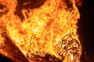 Büyük bir alev ahşap yapıyı yutar ve alevler gece gökyüzüne yükselir. Yoğun ateş, yangının yıkıcı gücünü gösteren sahneyi aydınlatıyor..