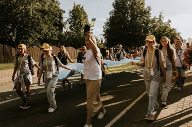 Bir grup insan, canlı bir şehir ortamında mesajlarını ifade eden pankartlar taşıyan bir şehir festivaline katılıyor. Sahne, arka planda çeşitli bir kalabalıkla festivalin enerji ve nişanını yakalıyor..