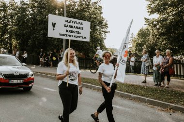 Bir grup insan, canlı bir şehir ortamında mesajlarını ifade eden pankartlar taşıyan bir şehir festivaline katılıyor. Sahne, arka planda çeşitli bir kalabalıkla festivalin enerji ve nişanını yakalıyor.. 