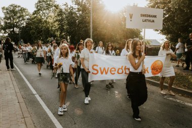 Bir grup insan, canlı bir şehir ortamında mesajlarını ifade eden pankartlar taşıyan bir şehir festivaline katılıyor. Sahne, arka planda çeşitli bir kalabalıkla festivalin enerji ve nişanını yakalıyor.. 