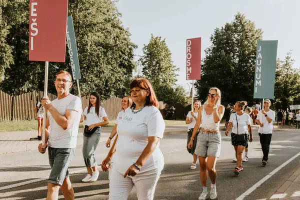 Bir grup insan, canlı bir şehir ortamında mesajlarını ifade eden pankartlar taşıyan bir şehir festivaline katılıyor. Sahne, arka planda çeşitli bir kalabalıkla festivalin enerji ve nişanını yakalıyor..