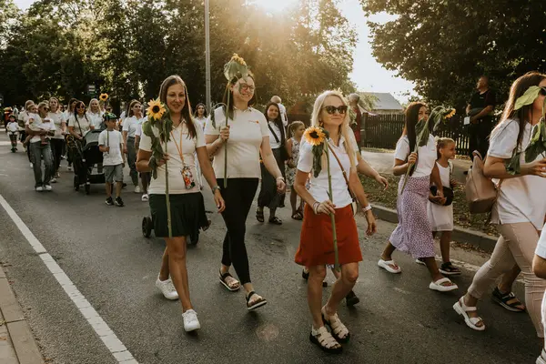 Bir grup insan bir şehir festivaline katılırken parlak çiçekler tutuyor. Renkli çiçekler, şehir zeminiyle tezat oluşturuyor. Bir kutlama anını yakalıyorlar..