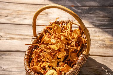 Kırsal dokuma sepetine istiflenmiş kurutulmuş yaban mantarlarının yakın çekimi, karmaşık dokularını ve doğal güneş ışığındaki altın renklerini gösteriyor..