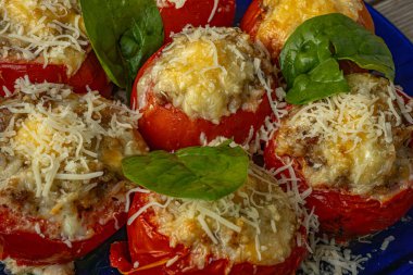 Baharatlı karışımla doldurulmuş, erimiş peynir ve ıspanak yapraklarıyla kaplanmış domateslerin yakın çekimi. Domatesler kızarana kadar kızarır..