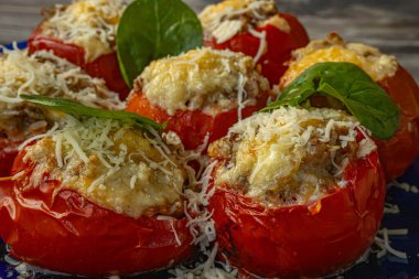 Baharatlı karışımla doldurulmuş, erimiş peynir ve ıspanak yapraklarıyla kaplanmış domateslerin yakın çekimi. Domatesler kızarana kadar kızarır..