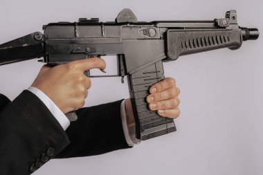 Siyah bir makineli tüfeğin ön sapını kavrayan bir elin yakın çekimi silahın vücudunun detaylarını gösteriyor. Görüntünün minimalist bir arka planı var, kopyalama alanı sağlıyor. Görünür bir logo yok.